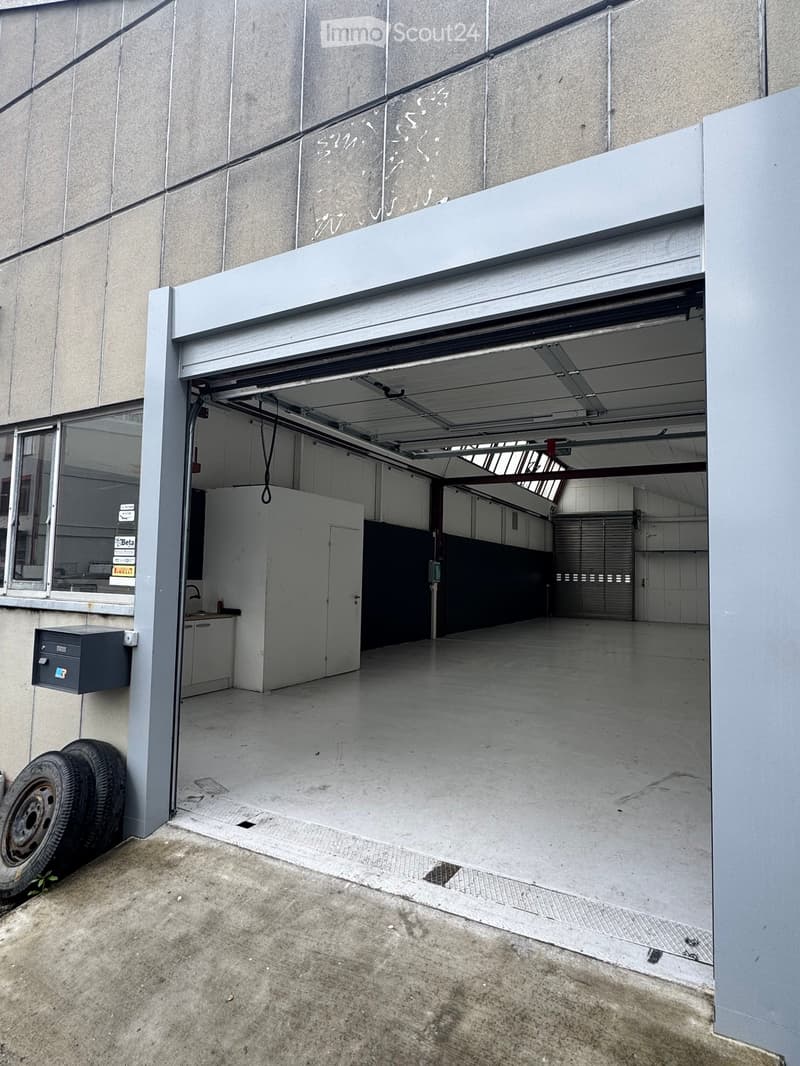 Building. Open garage with concrete floor, white walls, and a small utility area with cabinets and a sink.