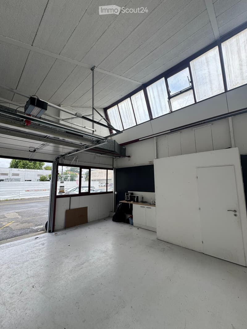 Unfurnished Room. Empty garage with concrete floor, large windows, and a small kitchenette area with cabinets and a microwave.