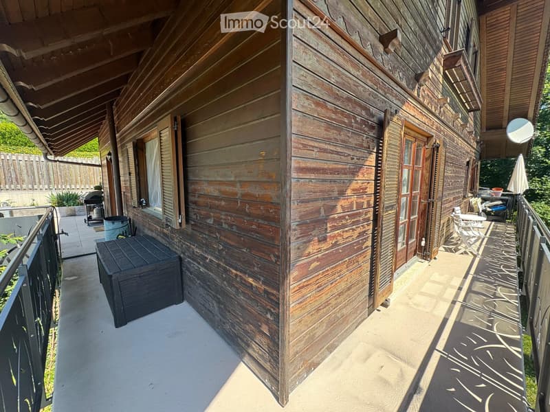 Wooden balcony with a rustic wooden wall, metal railing, and outdoor furniture including a table and chairs.