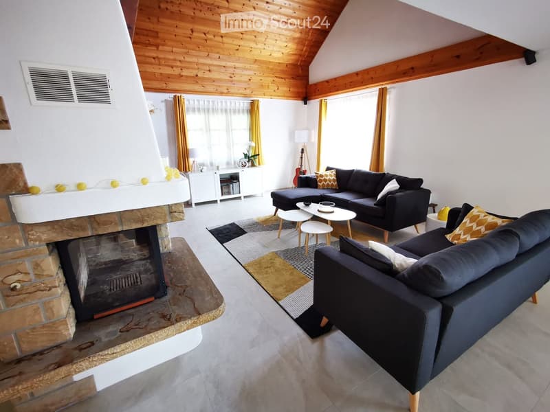 Modern living room with a dark grey sectional sofa, coffee table, small stools, a fireplace, and a guitar in the corner.