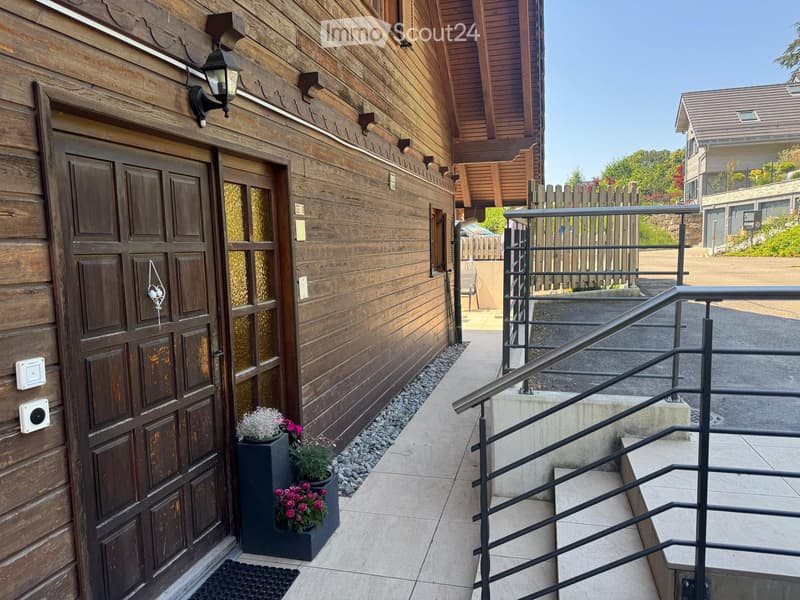 Wooden building entrance with a garage door, small potted plants, and a staircase leading upwards.