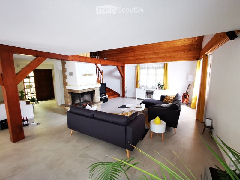 Spacious living room with exposed wooden beams, fireplace, grey sofa, coffee table, armchair, guitar, and decorative items.