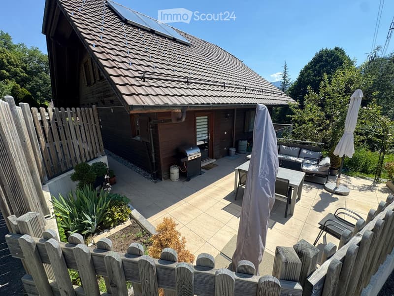 Outdoor patio area with a wooden fence, tiled floor, patio furniture including a table, chairs, and a sofa, along with a covered umbrella and a grill near the house.