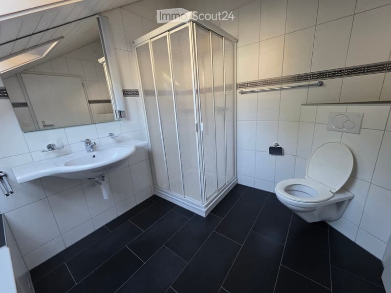 Modern bathroom with white tiles, black floor, sink, toilet, mirror, and glass-enclosed shower.