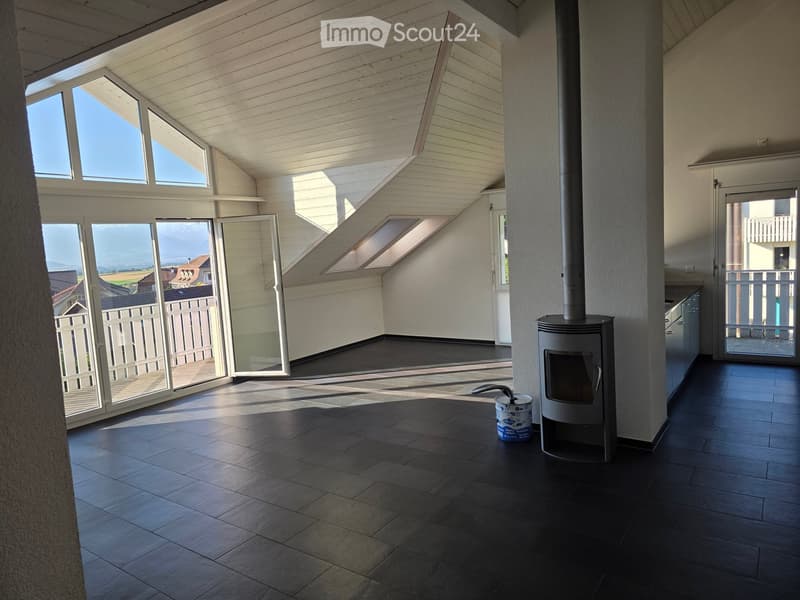 Modern, well-lit room with dark tiled flooring, wood stove, large windows, and sliding glass doors leading to a balcony.