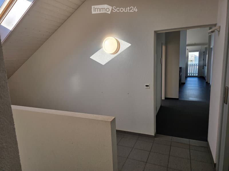 A modern hallway with white walls, tiled flooring, and a built-in light fixture. The hallway leads to an open area with a visible balcony or terrace beyond.