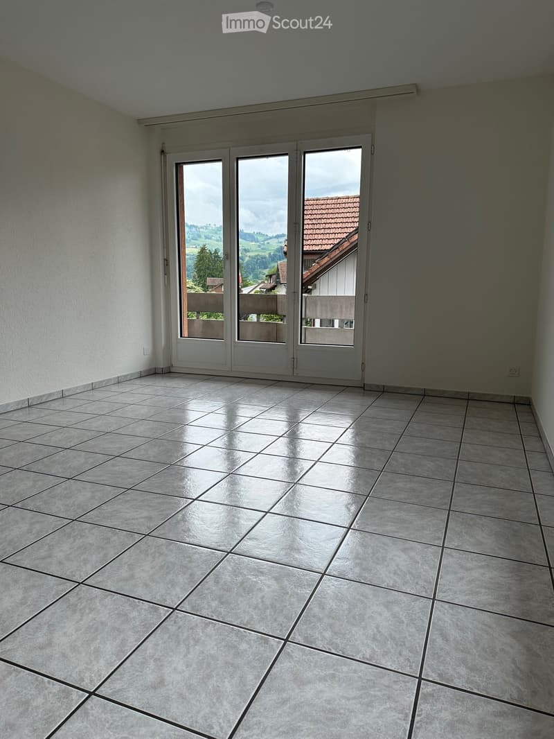 Empty room with tiled floor and large sliding glass doors leading to a balcony with a scenic view of the countryside.