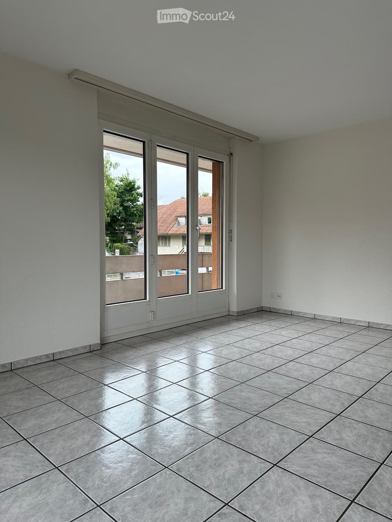 Empty room with tiled floor, white walls, and large sliding glass doors leading to a balcony or outdoor area.
