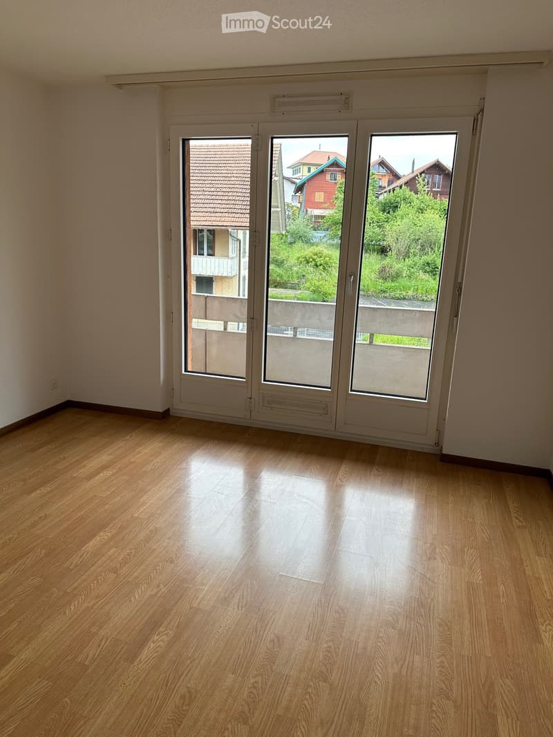 Empty room with wooden flooring and large sliding glass doors leading to a balcony or outdoor area. The walls are painted a light color, and the space is well-lit with natural light.