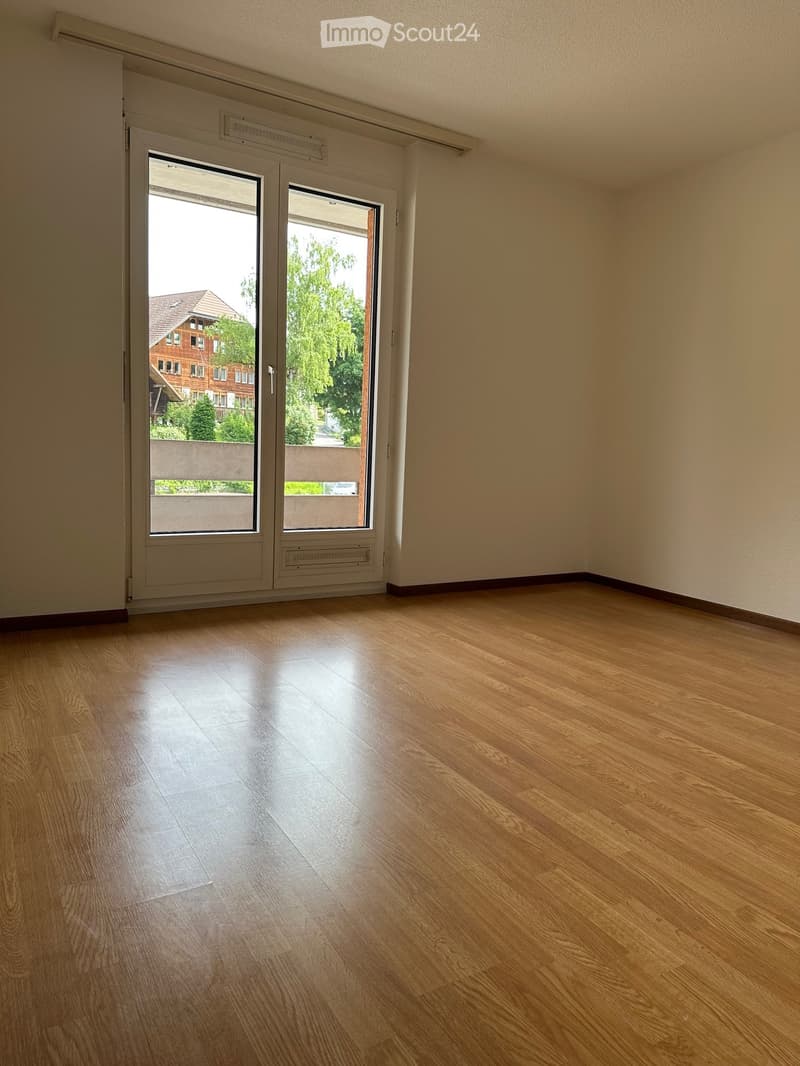 Empty room with wooden flooring and large sliding glass doors leading to a balcony or outdoor area. The walls are painted a light beige color, and the room has a simple, clean design with no visible furniture or decorations.