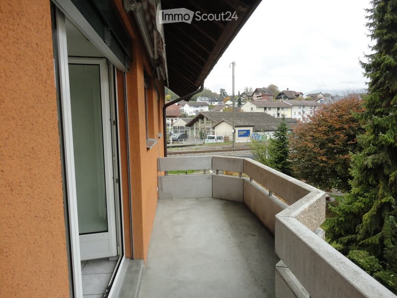 Balcony with concrete floor, white railing, and view of residential area with trees and houses.