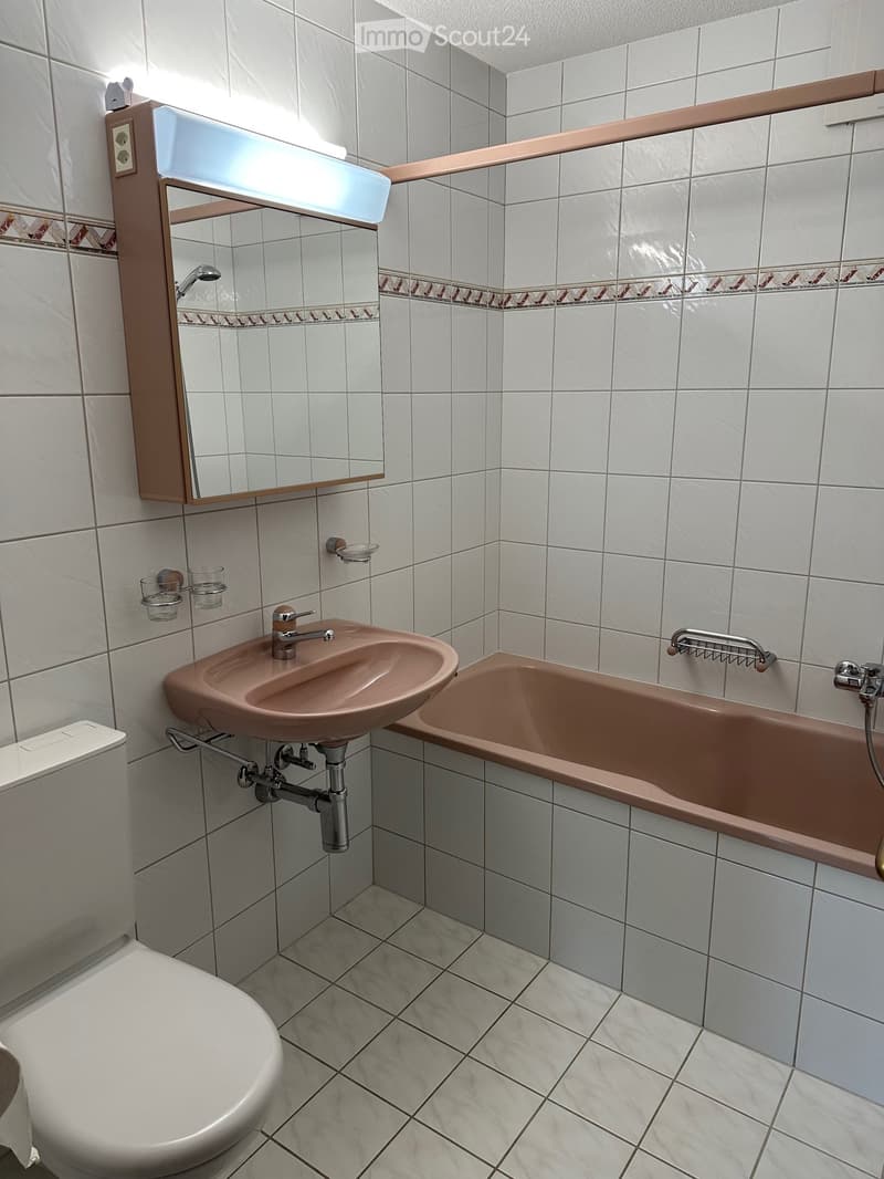 Bathroom with white tiled walls and floor, featuring a toilet, sink, bathtub, mirror, and decorative tiles.