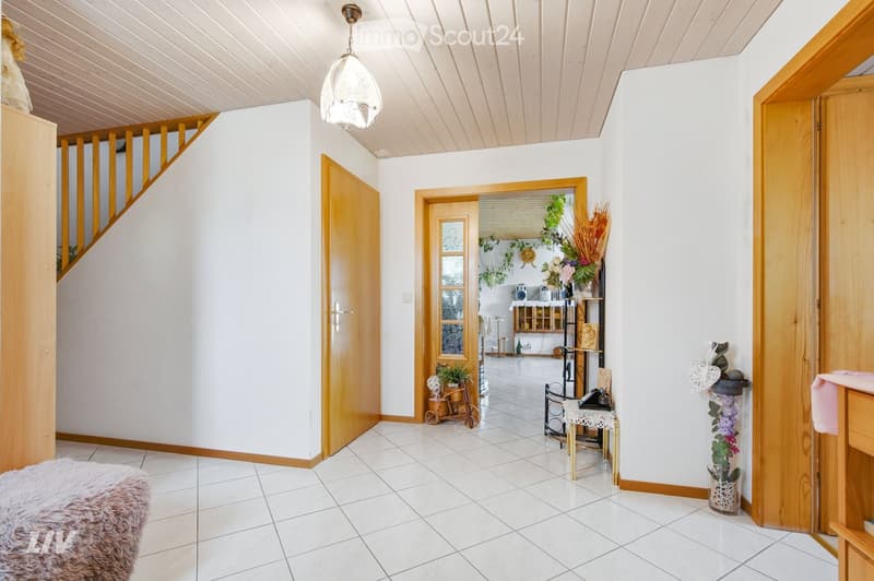 Hallway with tiled floor, wooden doors, staircase, small table with chair, decorative plants, and vases.