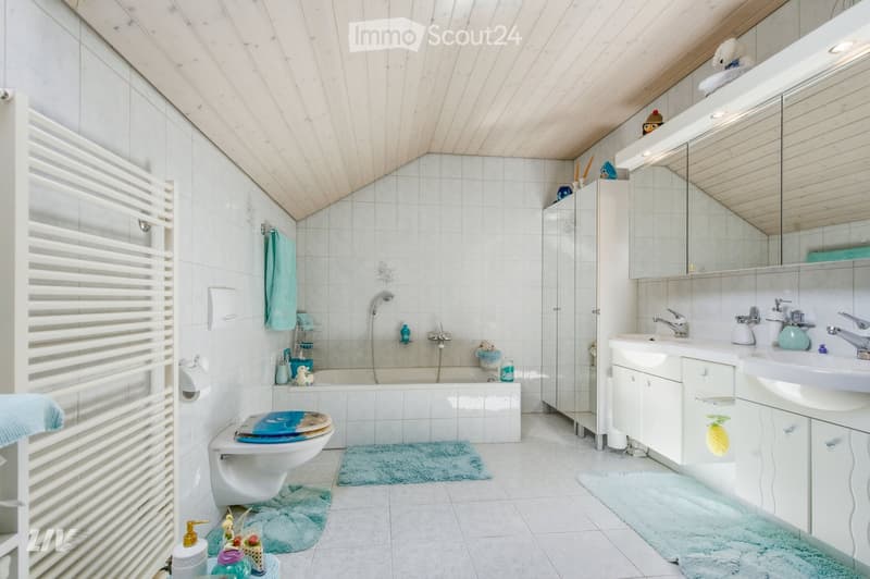 Bright, modern bathroom with white tiles, a bathtub, toilet, double sink, and a large mirror. Features include a shower area, towel racks, and decorative items.