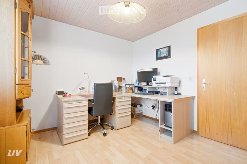 A well-organized home office with a wooden desk, ergonomic chair, computer setup, and a large window providing natural light.