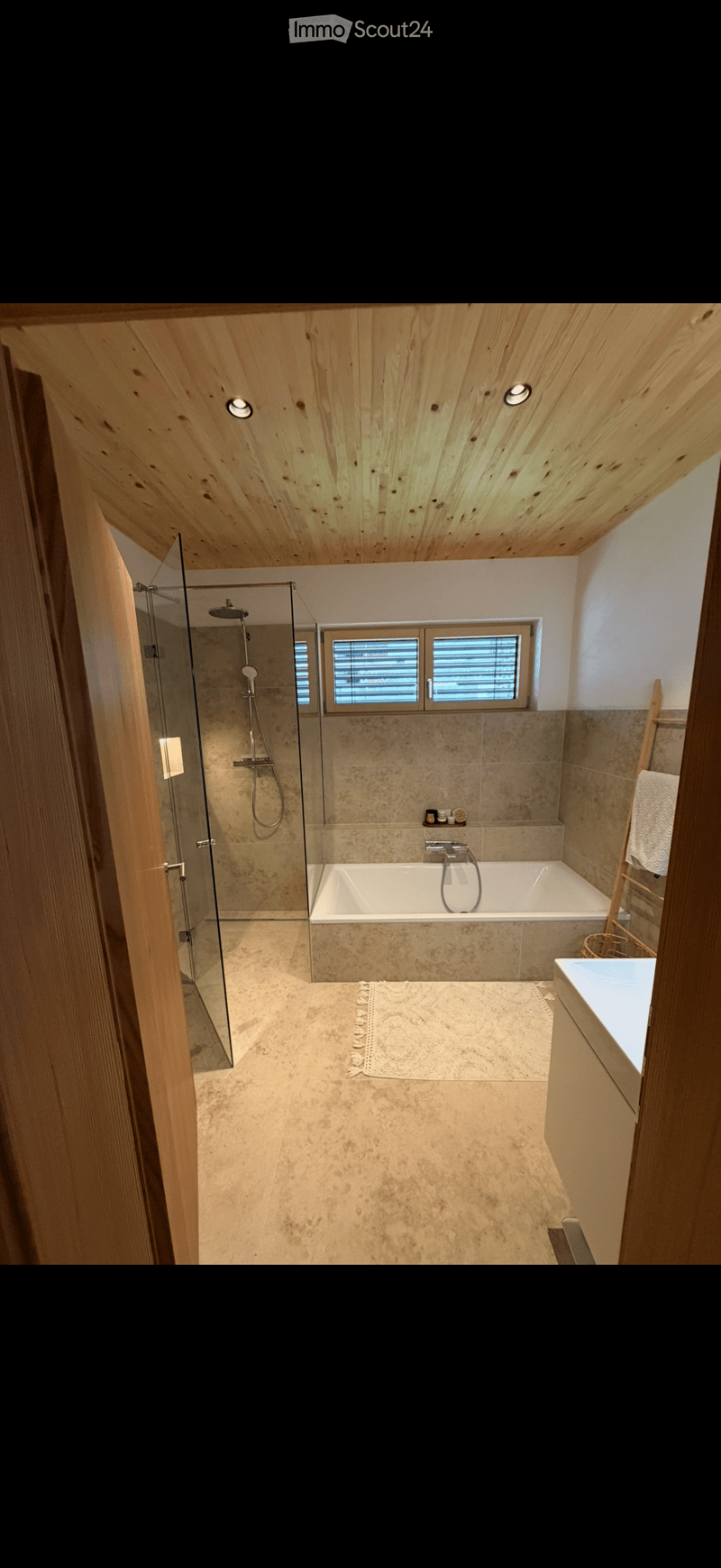 Modern bathroom with a bathtub, glass-enclosed shower, sink, and wooden ceiling with recessed lighting.