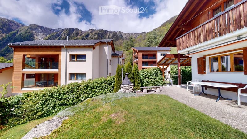 A well-maintained garden area with a lawn, patio furniture, and a scenic mountain view in the background.
