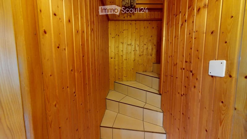Wooden-paneled hallway with a staircase leading upwards, featuring light-colored tiled steps and a small shelf at the top.