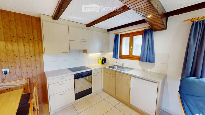 Modern kitchen with white cabinets, granite countertops, stainless steel sink, and built-in oven. Wooden dining table and chairs are visible in the foreground.