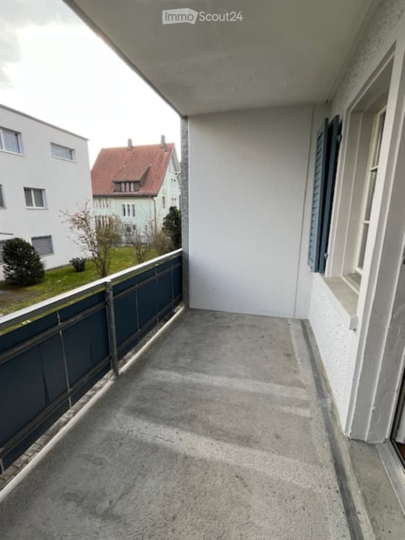 Empty balcony with concrete floor, metal railing, and view of neighboring buildings and greenery.