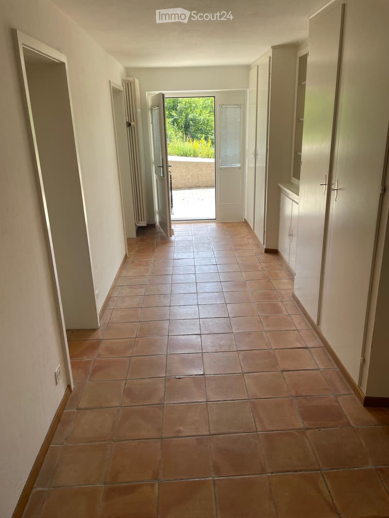 Empty hallway with tiled floor, white walls, and several doors leading to other rooms and an outdoor area.