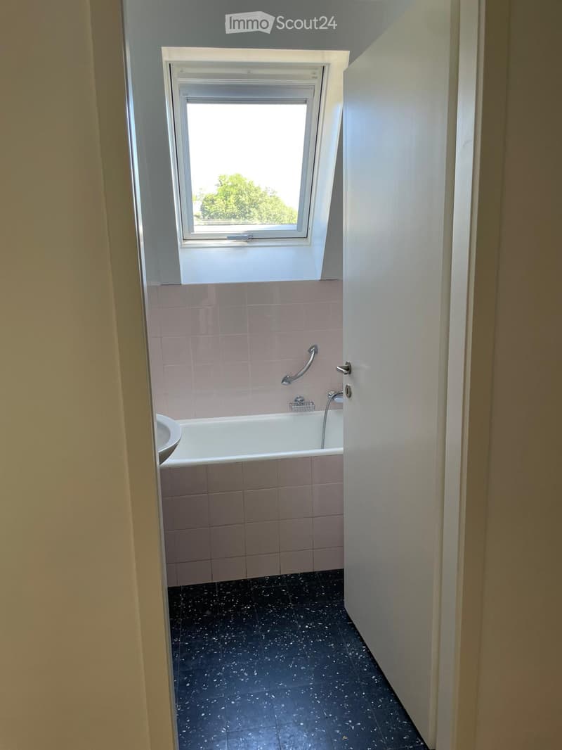 Bathroom with a bathtub, sink, and a window above the tub. The walls are tiled in light pink, and the floor is dark with a speckled pattern.
