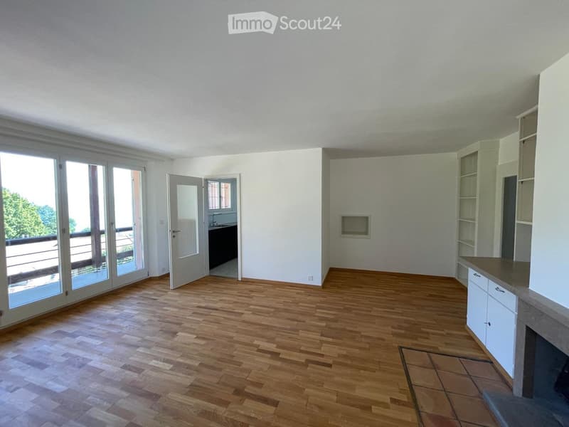 Empty room with wooden flooring, white walls, large sliding glass doors leading to a balcony, and a small adjacent bathroom area.