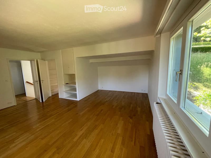 Empty room with wooden flooring, white walls, built-in shelving unit, and large window with radiator below.