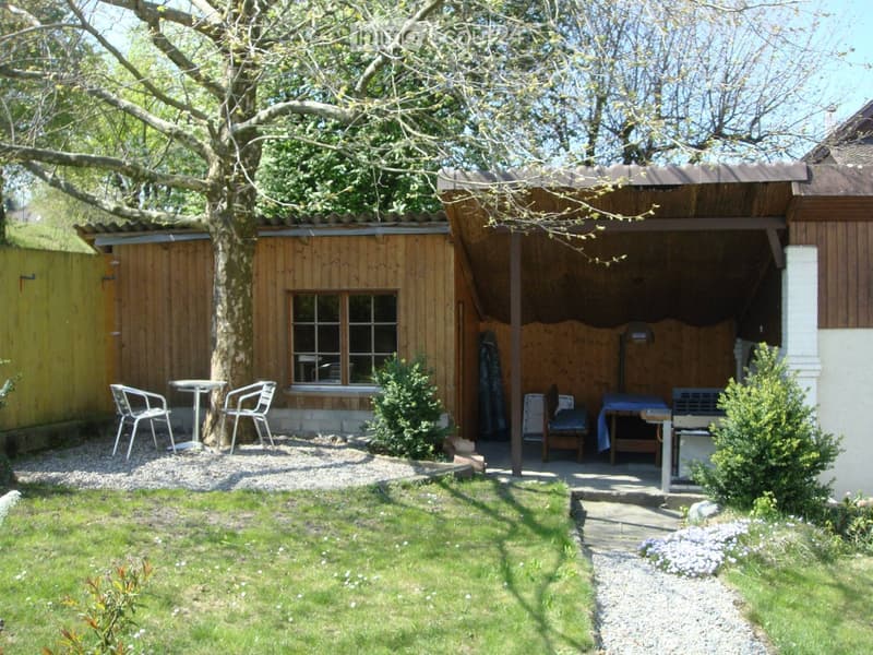 Garden area with a wooden shed, seating area, and a covered patio with a table and chairs.