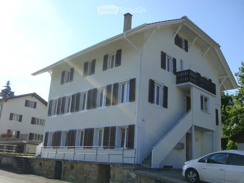 Two-story white house with multiple windows, balconies, and a raised ground floor entrance.