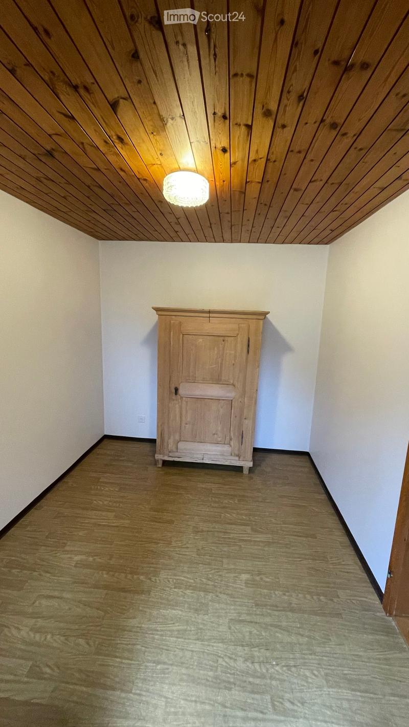 Empty room with wooden floor, white walls, and a single wooden cabinet. The ceiling has wooden paneling and a light fixture.