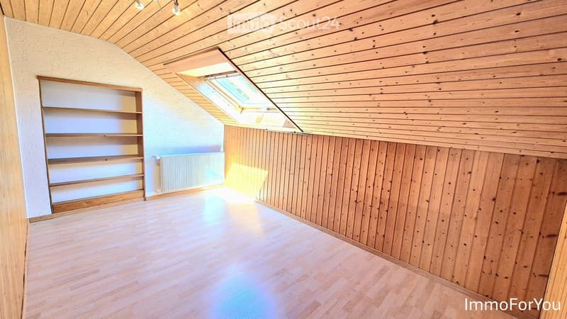 Empty attic room with wooden walls, ceiling, and floor, featuring built-in wooden shelving and a skylight window.