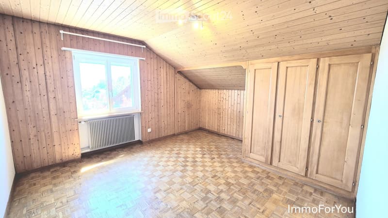 Empty room with wooden walls, wooden floor, large window, radiator, and built-in closet.