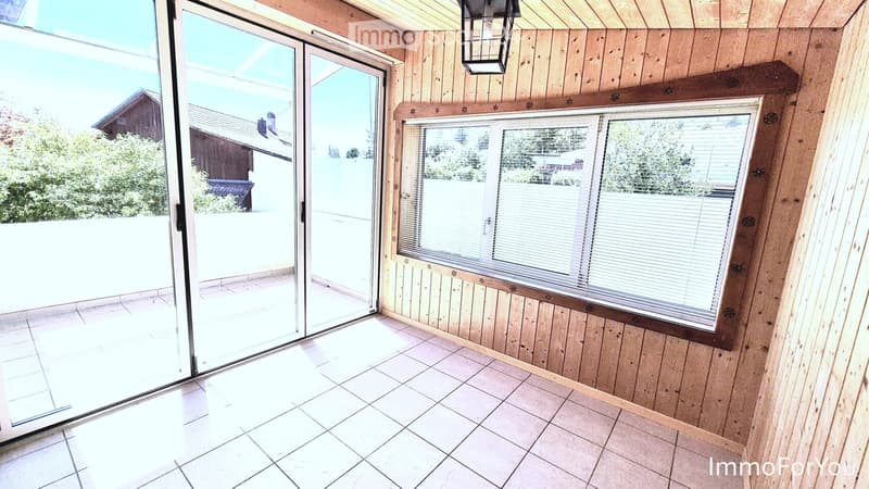 Empty room with wooden walls, tiled floor, large sliding glass door leading to a patio, and a window with blinds.