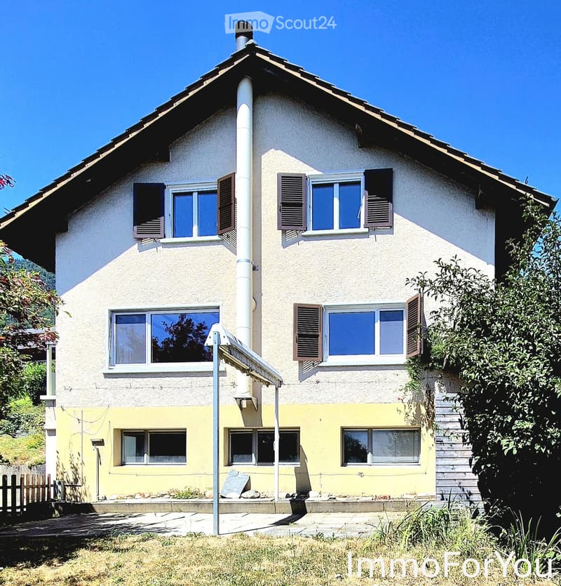 Two-story house with white and yellow exterior, multiple windows with shutters, and a small garden area.