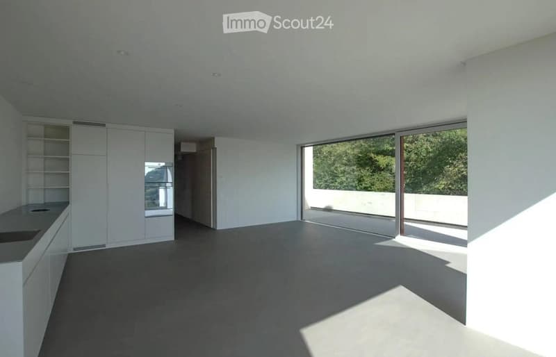Open-plan unfurnished room with white cabinetry, a built-in oven, and large sliding glass doors leading to a balcony.