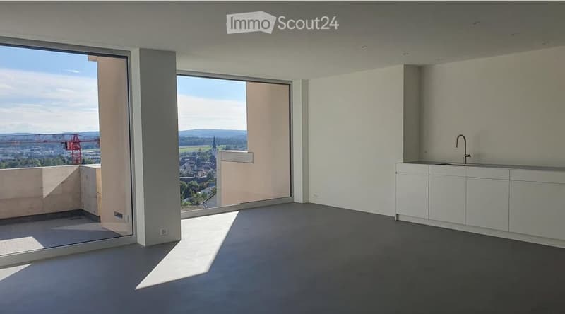 Modern, unfurnished room with large windows offering a scenic view, white cabinetry, and a sleek sink.