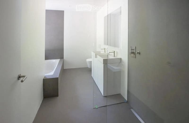 Modern bathroom with a bathtub, two sinks, a toilet, and a large mirror. The space features a glass partition and neutral tones.