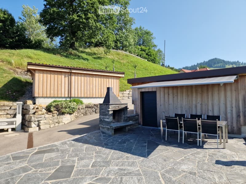 Outdoor patio area with stone flooring, wooden structures, a stone fireplace, and a dining set including a table and chairs.