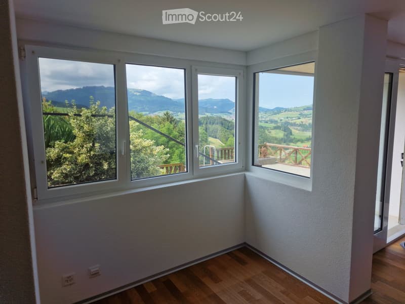 Empty room with wooden flooring, white walls, and large windows offering scenic mountain views.