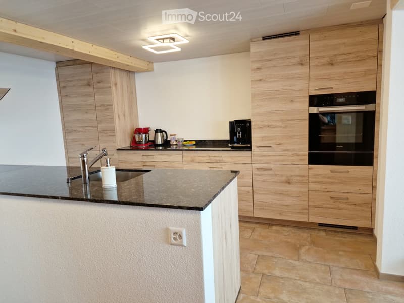 Modern kitchen with light wood cabinets, black countertops, stainless steel sink, and various appliances including a coffee maker and stand mixer.