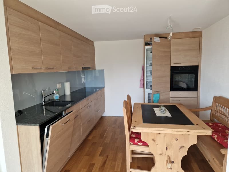 Modern kitchen with wooden cabinets, granite countertop, sink, oven, and a small dining area with a wooden table and chairs.