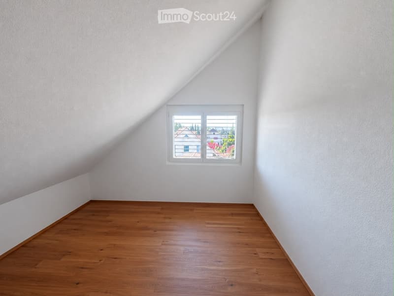 Empty attic room with wooden flooring and white walls, featuring a single window with white frame and blinds.