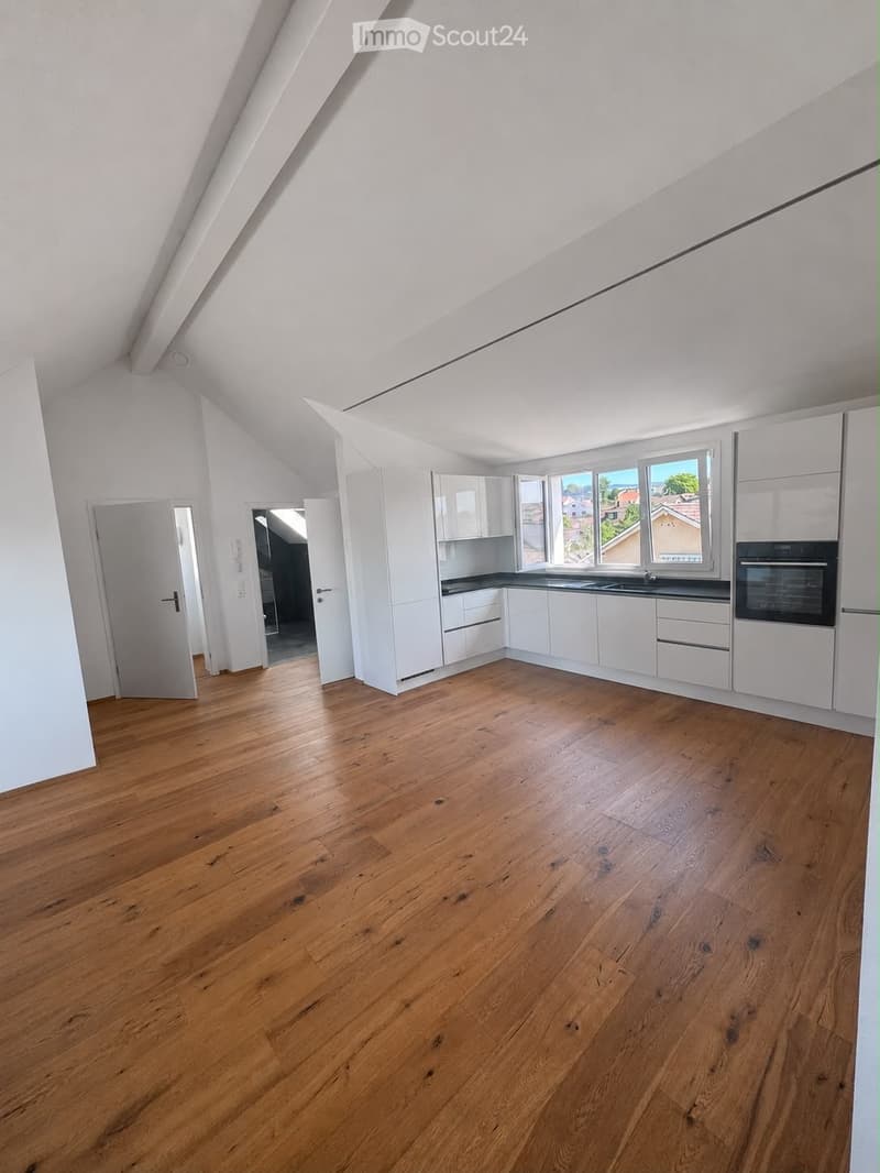 Empty kitchen with white cabinets, wooden flooring, and large windows offering a view of the outside. The space is clean and unfurnished, with no appliances or furniture present.