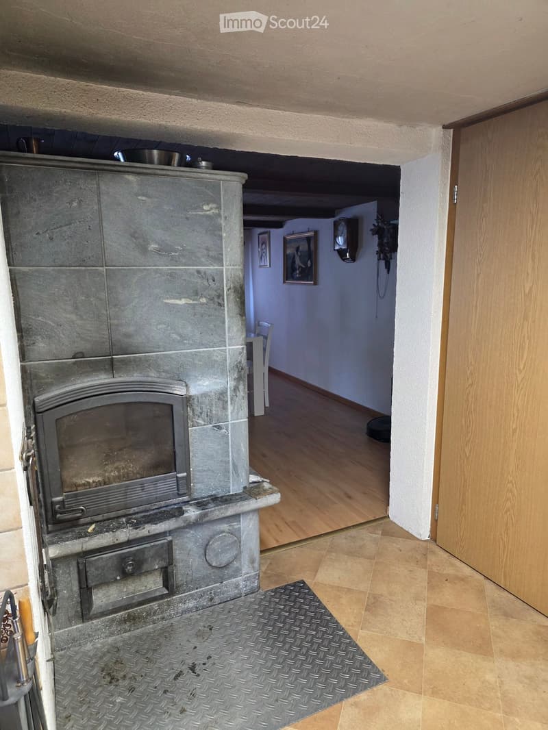 Hallway with a stone fireplace and a view into another room with a wooden floor and a white chair.