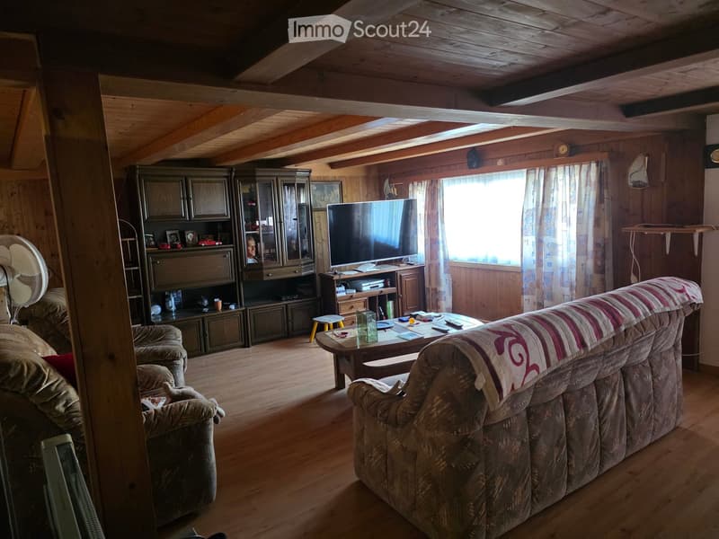Cozy living room with wooden walls and ceiling, featuring a sofa, coffee table, armchair, TV, and wooden cabinet.