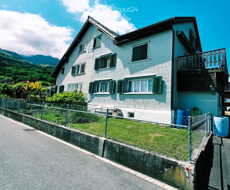 Two-story white brick house with green shutters, balcony, and scenic mountain view.