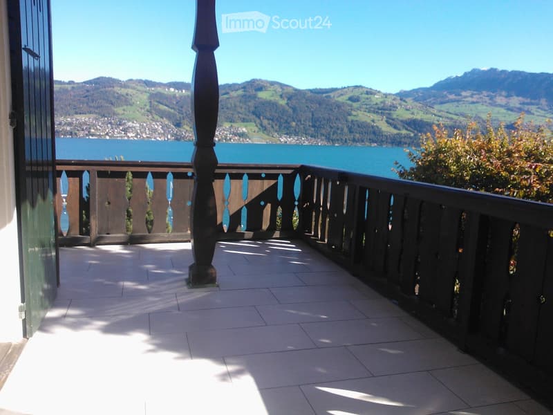 Balcony with tiled floor, wooden railing, and scenic view of a lake and mountains.
