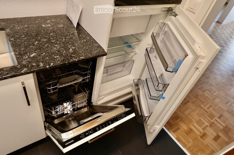Open kitchen area with a stainless steel Siemens dishwasher, white cabinets, and a granite countertop.
