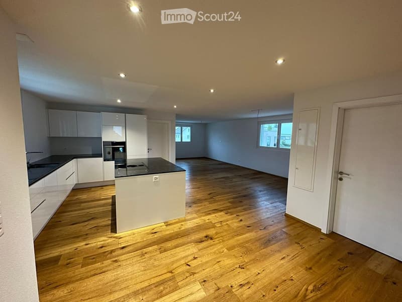 Modern kitchen with white cabinets, a central island, and wooden flooring. The space is open and well-lit with recessed lighting.